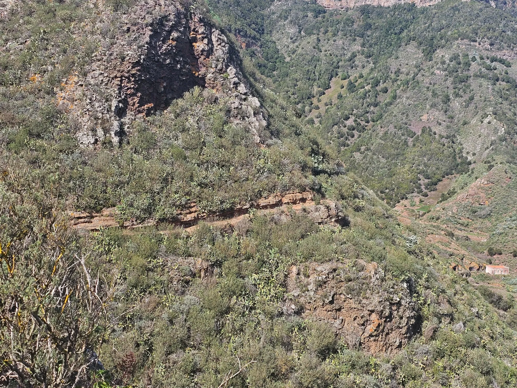 Deeply eroded ridges and abandoned terraces in the Anaga massif, with a single white house far below in the valley