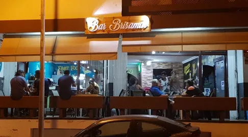 The lit sign and open frontage of Bar Brisamar at night, with people sitting at the bar counter inside