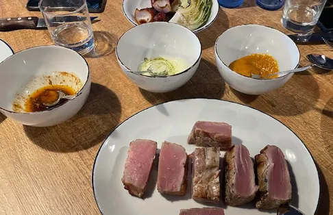 Slices of seared rare tuna on a white plate, with bowls of mojo and other sauces on a wooden table