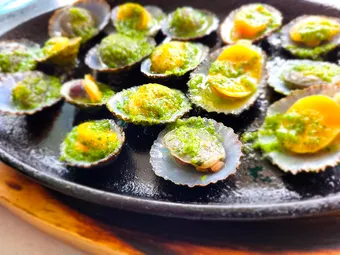 A hot metal platter of limpets — lapas — in their shells, covered in green mojo, with lemon