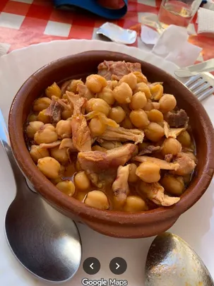 Garbanzas — chickpea stew with pork — served in a brown earthenware bowl on a red checked tablecloth