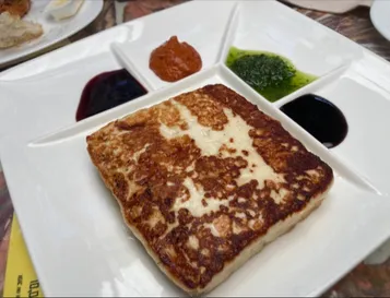 A slab of grilled Canarian cheese on a plate, served with red and green mojo and two fruit preserves