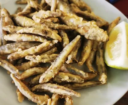 A plate of small whole fried fish, lightly floured, served with a lemon wedge