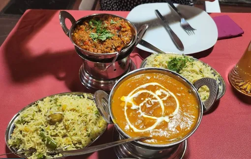 Indian curries in copper balti dishes with two pilau rices, on a red tablecloth