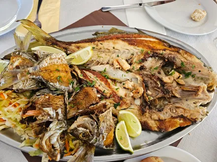 A large metal platter of mixed grilled and fried fish with lemon wedges on a bed of salad