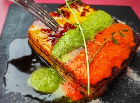 A layered potato and vegetable terrine on slate, striped with red and green mojo sauces and finished with herbs